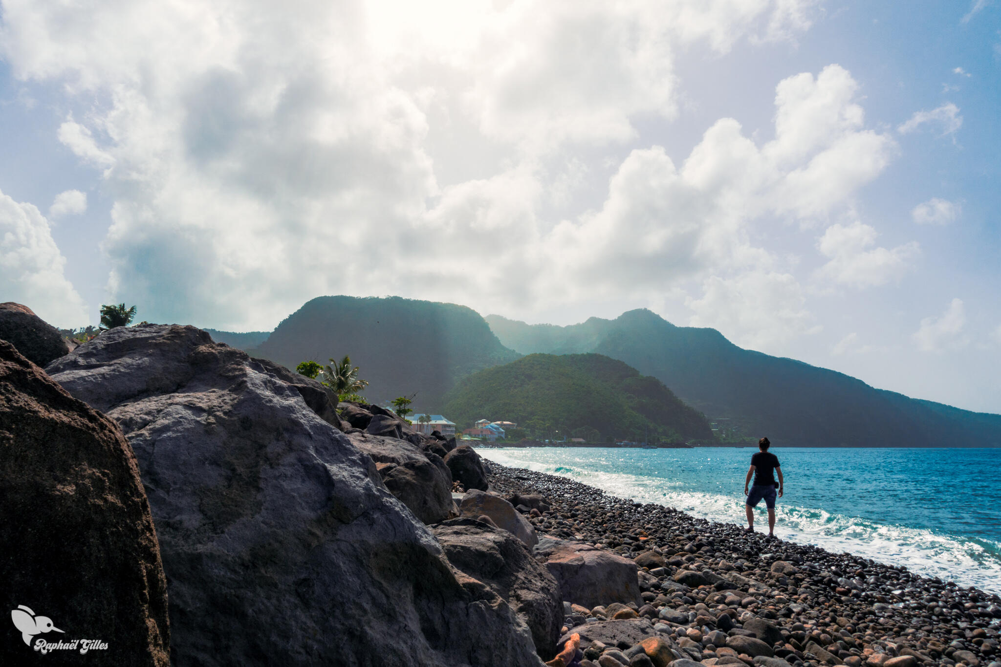 Un homme en train d’observer des montagnes au bord de la mer.