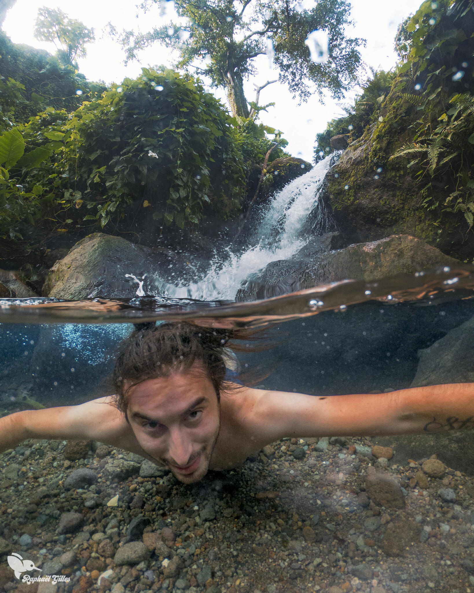 Un homme sous l’eau, une cascade en arrière plan.