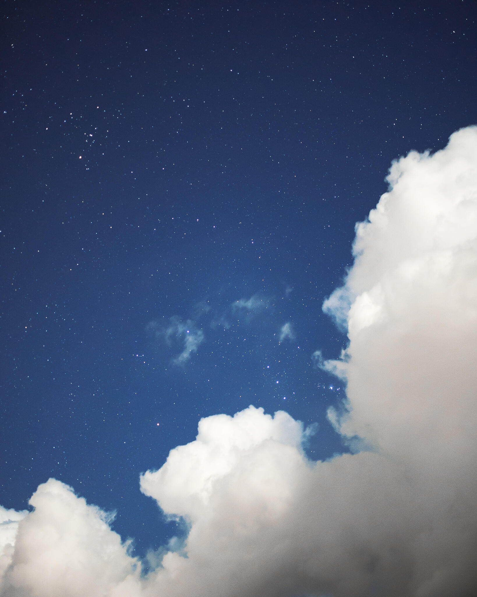 Un ciel étoilé. Des nuages blancs en premier plan.