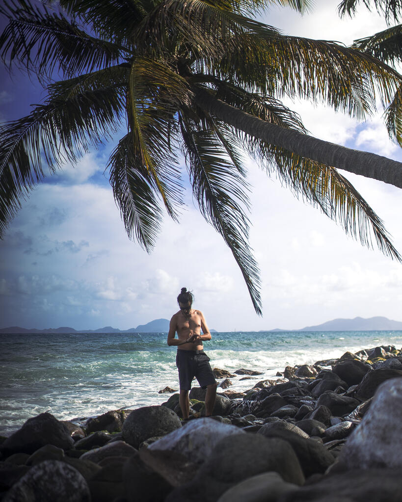 Un homme sous un cocotier au bord de la mer. Des îles en fond.