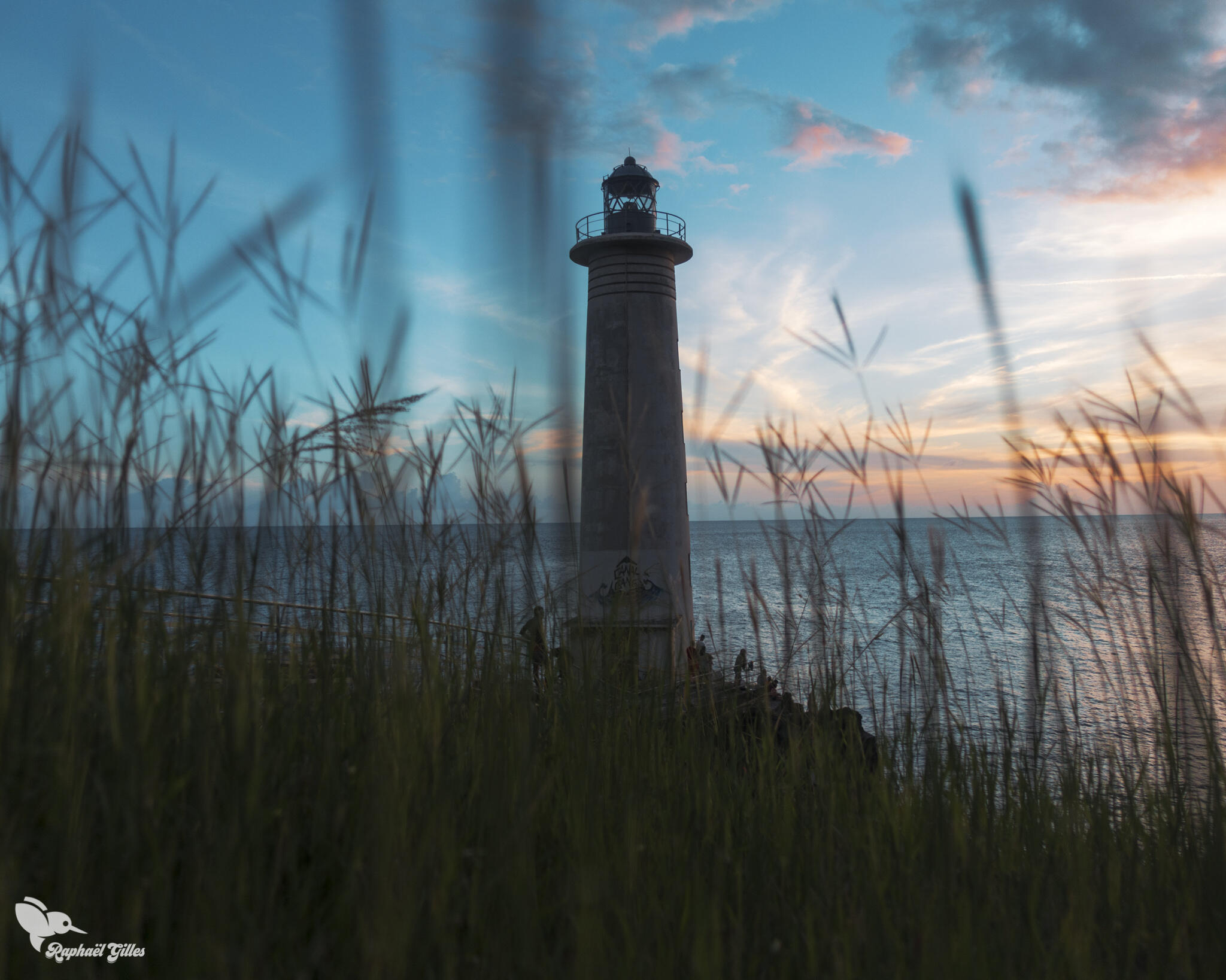 Le soleil se couche sur une mer calme. Un phare au premier plan.