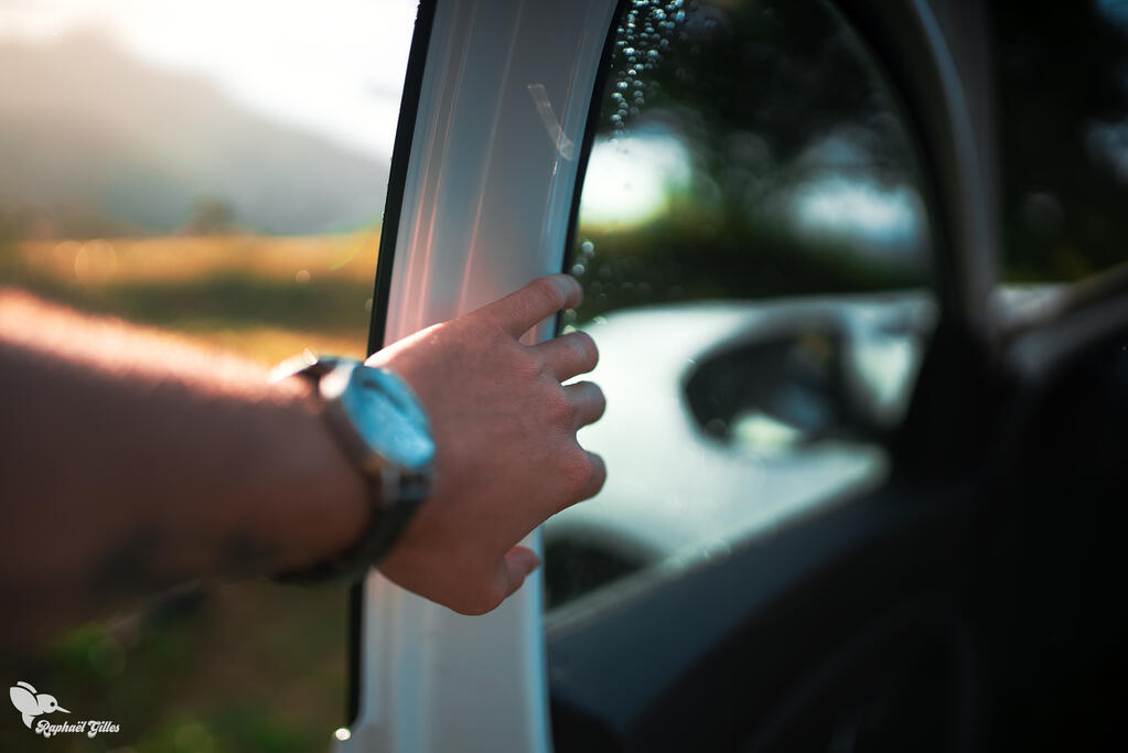 Photo prise à la première personne. Une main d'homme portant une montre ouvre la portière d'une voiture blanche.